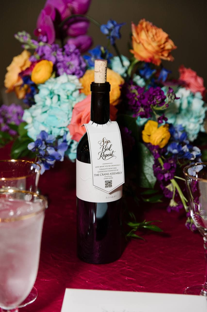 Close-up of a shaped wine bottle neck tag with Sip Bid Repeat lettering and a QR code