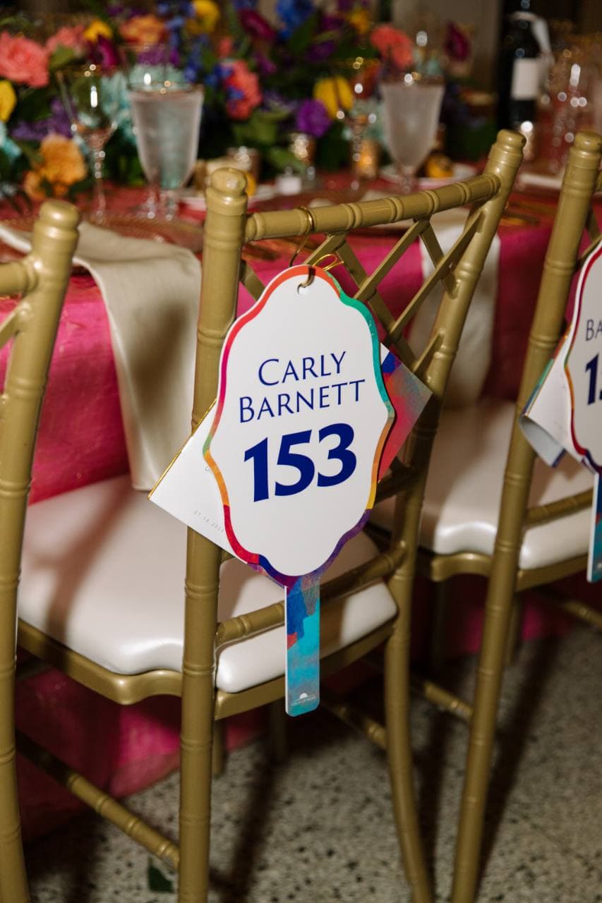 Personalized auction paddle with a guest name and bidder number hanging on a chair